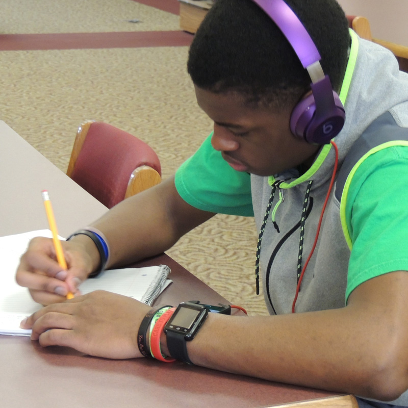 student with headphones on while writing in a notepad