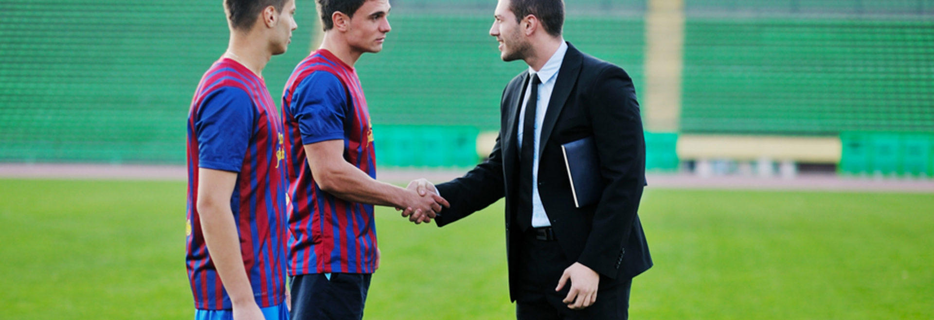 two sports players shaking a business mans hand