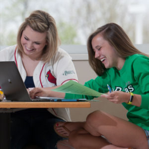 two girls smiling in front of a laptop