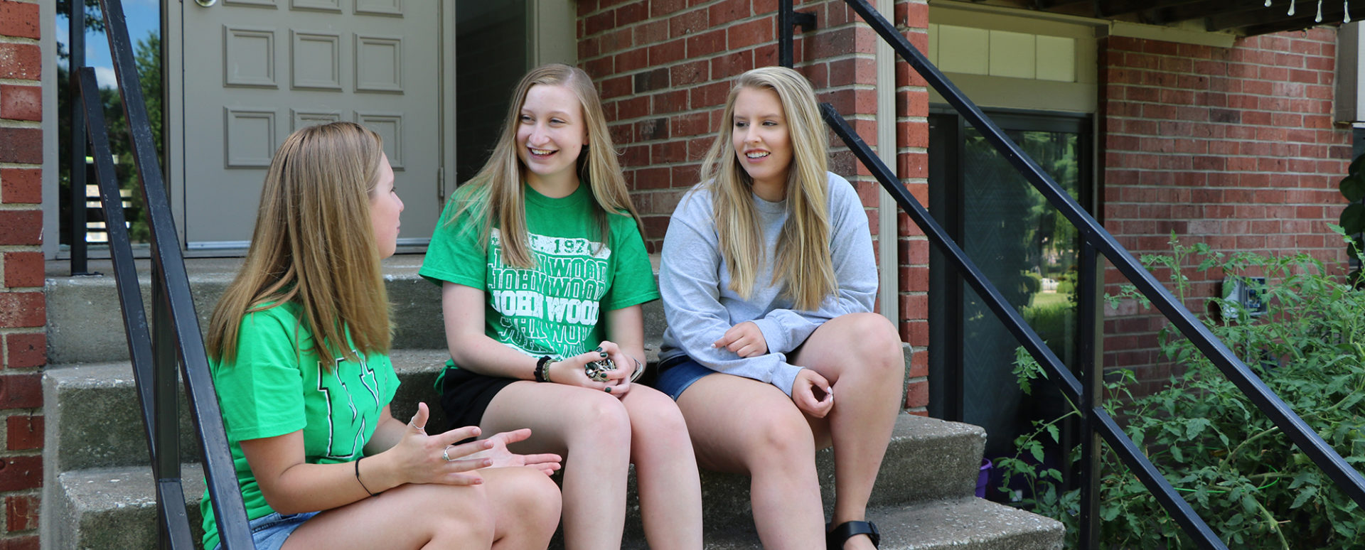 Three students sit on stairs in front of an apartment