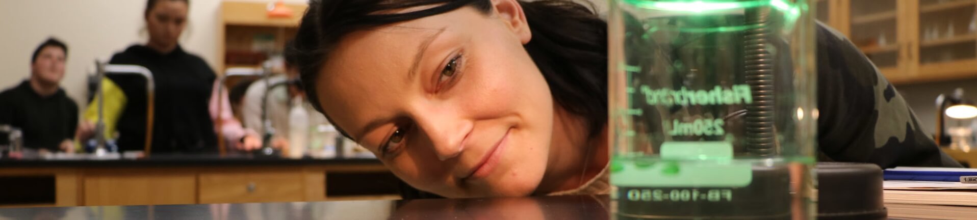 Student's chin nears desk as she observes the amount of liquid in a beaker