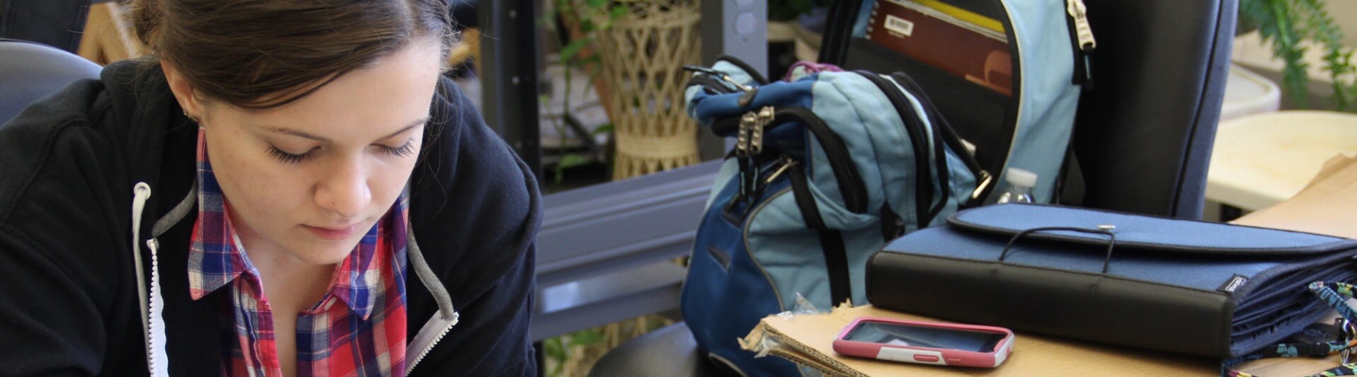 Student pauses at table for study notes with her open backpack