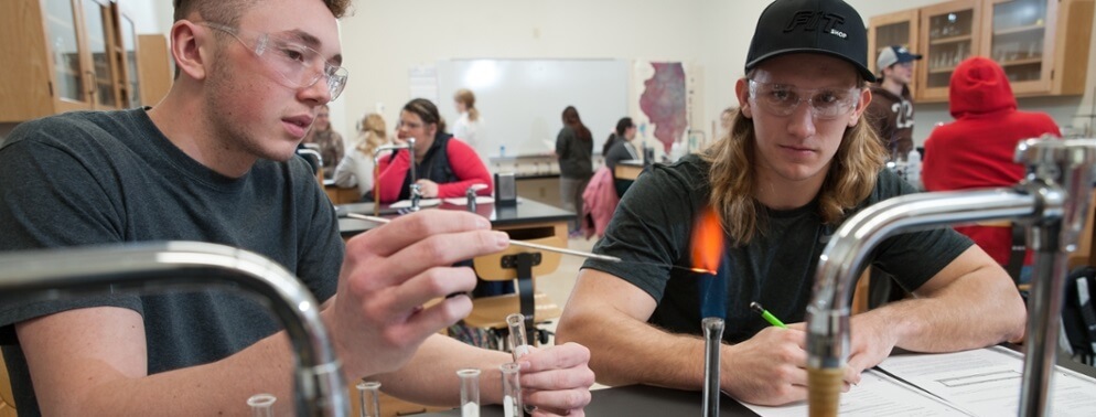 Two chemistry students work with a burner