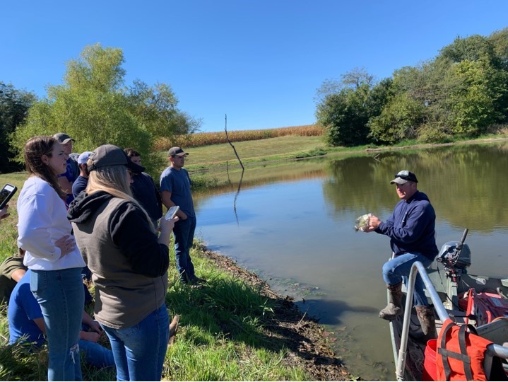 Instructor demonstrates holding a fish to students in pond