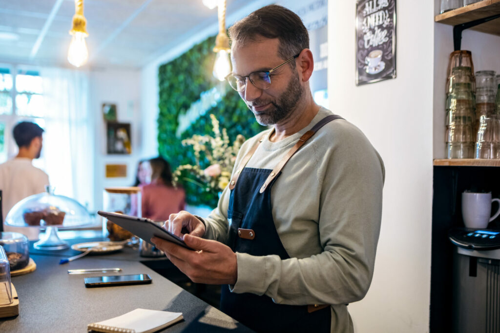 Handsome mature owner bakery working while pointing order delivery in a digital tablet in a healthy pastry shop.